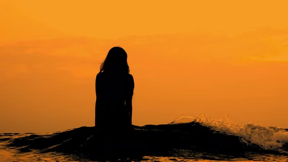 Woman In Silhouette Walking Waist Deep Into Golden Sea At Sunset alt