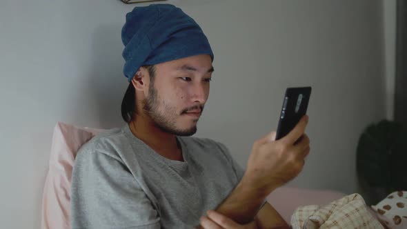 Handsome Asian man using a Smartphone while Lying on Bed at home.