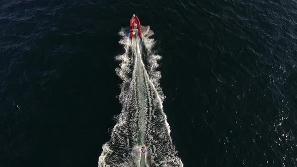Red Inflatable Boat with Man on Oit Pulling Another Male on Board in Sea alt