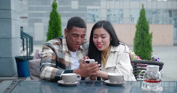 Two Charming People in Casual Cozy Clothes Sitting at the Table in a Summer Terrace of a Cafeteria alt