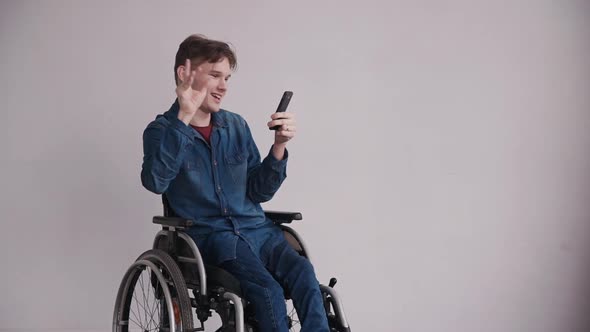 Young Man in Wheelchair Using Modern Smartphone at Home