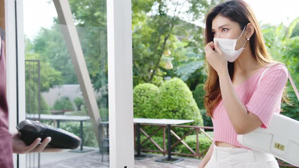 Young Asia female customer wear face mask contactless credit card payment and take out food bag. alt