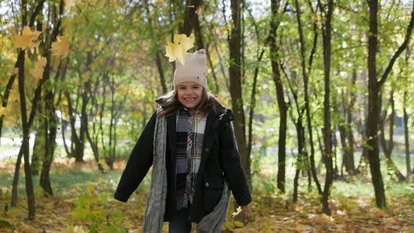 Happy Girl Drops Autumn Leaves in a Park