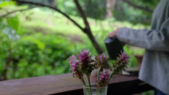 a woman pouring hot water from kettle to make drip coffee with pink flower in foreground