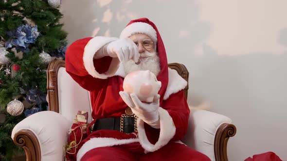 Santa Claus putting coin into a ceramic piggy bank. Savings concept for the end of the year.