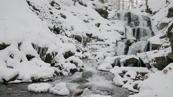 Wonderful frozen foot of a waterfall with a powerful stream of water at winter carpathian mountains alt