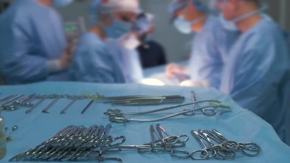 Closeup of Surgical Tools on Table and Team of Surgery Doctors Operating a Patient in Hospital Room alt