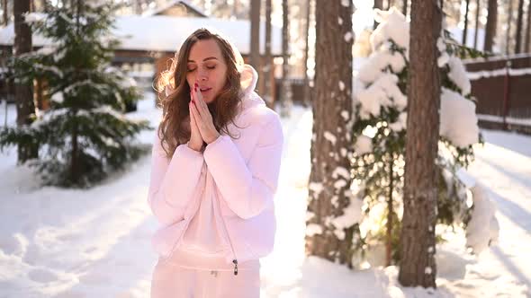Winter Sunny Cold Portrait in Snowfall of Beautiful Young Woman in a White Warm Outwear Down Jacket