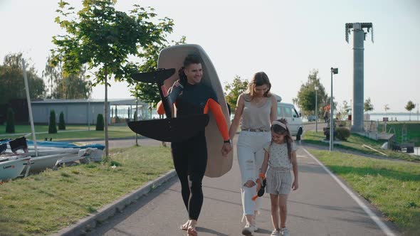 Man Walk with His Family Carrying a Surfboard to the Lake Shore on a Sunny Day alt