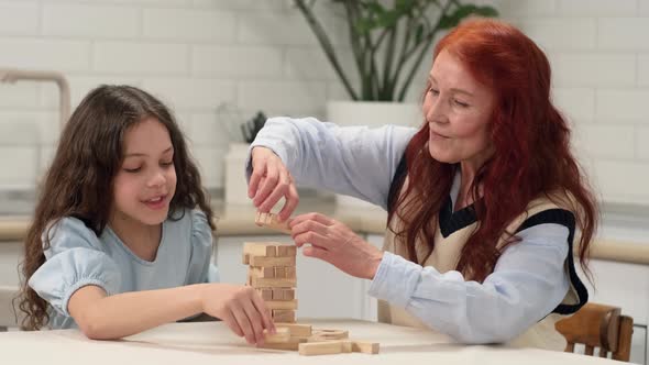 Grandmother and Granddaughter Play a Board Game at Home Build a Tower From Wooden Blocks alt