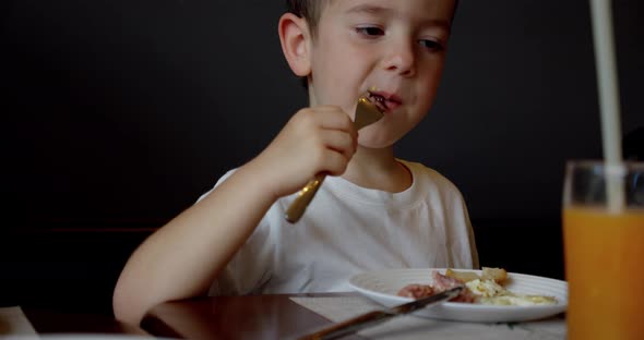 Cute Healthy Preschool Kid Boy Eats Eag and Pasta Noodles Sitting in Nursery Cafe alt