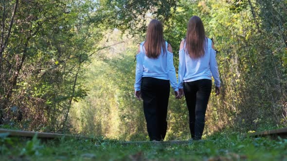 Twins Girls Holding Hands Walking Along Railroad Tracks alt