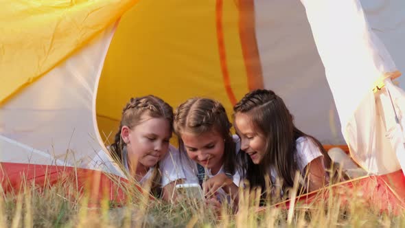 Beautiful girls gossip lying together in a tent while camping in the summer forest during summer alt