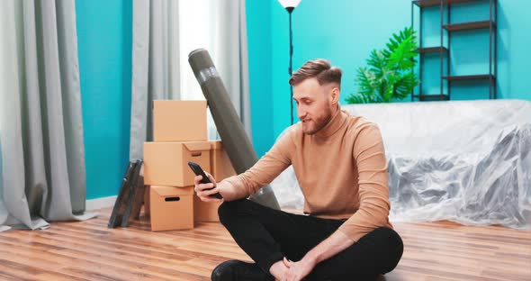 Puzzled Man Look at Smartphone Device Relocate in New Apartment Search Furniture for Their Flat alt