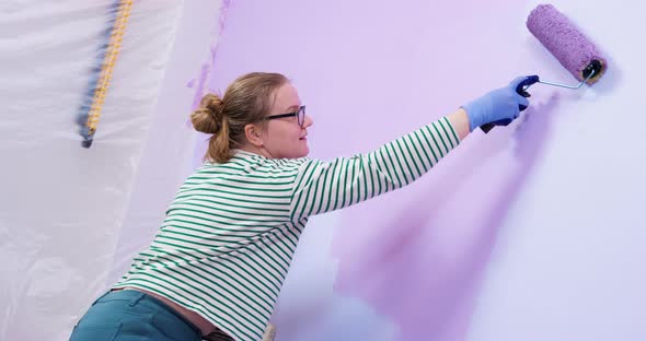 Happy Woman Makes Repairs in a New Home Paints the Walls alt