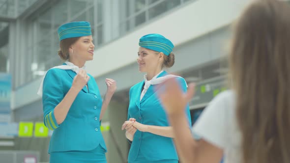 Blurred Caucasian Little Girl Waving To Beautiful Stewardesses in Blue Uniform. Two Confident Slim alt