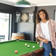 A young African American man with curly hair stands by a pool table with copy space - PhotoDune Item for Sale