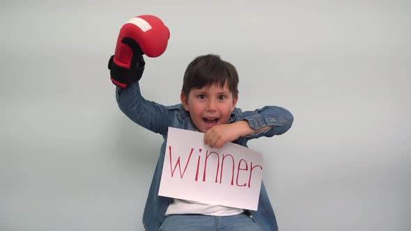 A Boy in Boxing Gloves Holds a Piece of Paper with the Inscription WINNER and Cheers A Joyful Child