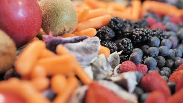 Tracking shot over fruit, berries, and vegetables arranged on cutting board. alt