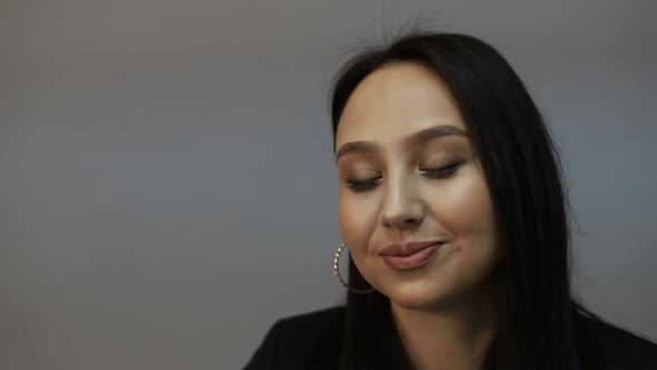Brunette european woman looking at camera while standing in the office on gray background alt