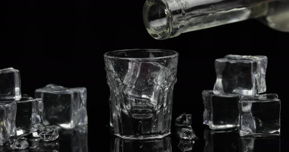 Pouring Up Shot of Vodka From a Bottle Into Glass. Black Background alt