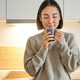 Portrait of smiling asian woman standing on her kitchen, drinking coffee and looking at camera - PhotoDune Item for Sale
