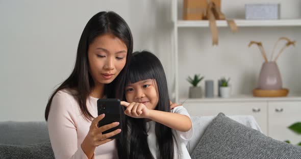 Happy Asian Single Parent Family Sitting on Couch Looking at Screen of Smartphone alt