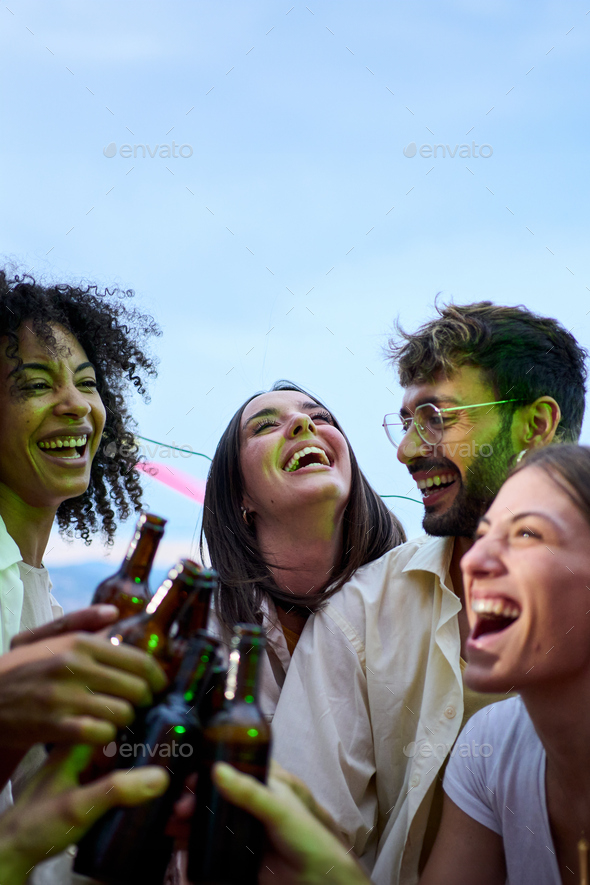 Cheerful multiracial young people toast with beer bottles gathered ...