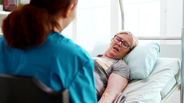 In Nursing Home Old Sick Lady Lying in Bed Talks with a Female Nurse alt