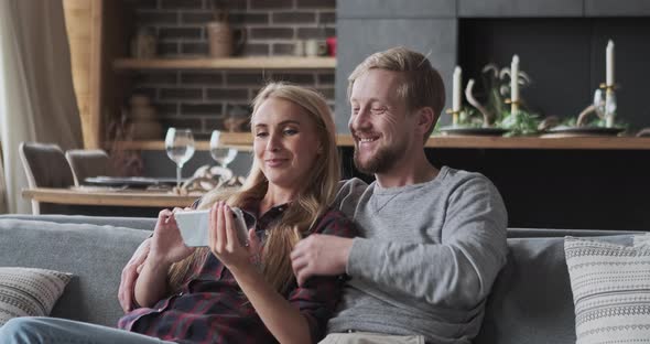 Happy Blonde Female and Male Enjoy Weekend Recreational Home Activity Watching Video Smartphone