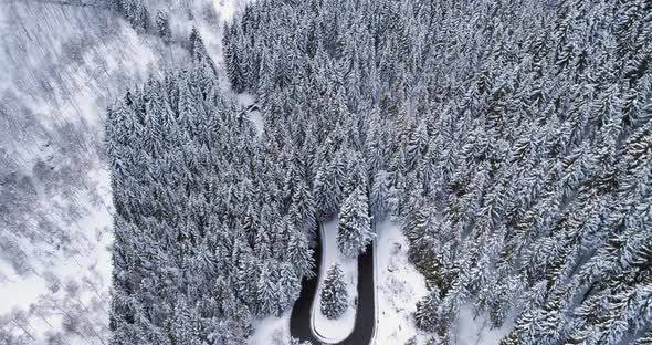 Forward Aerial Top View Over Car Travelling on Hairpin Bend Turn Road in Mountain Winter Snow
