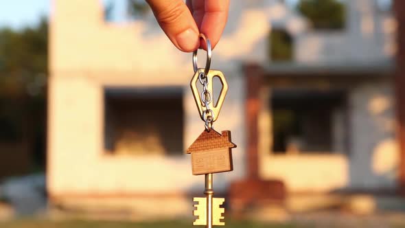 Hand with the key to the future house on the background of a construction site and walls alt