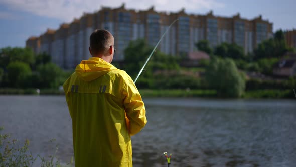 Back View Fisherman Catching Fish in River in Slow Motion with Blurred Urban House at Background on alt