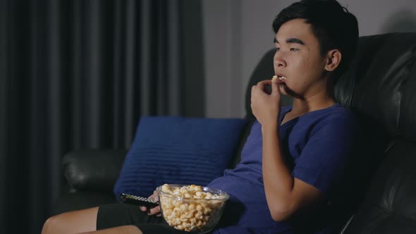 young man eating popcorn while sitting on a couch and watching TV at night