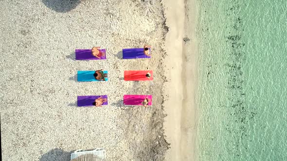 Aerial view of group of people doing yoga on colourful mats on the beach. alt