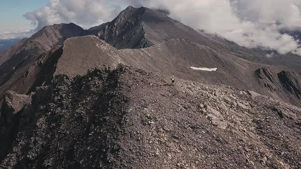 Mountain Aerial Flight Above Man Hiking Along Rocky Trail Path in Sunny Day