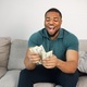 Black guy sitting on a couch in living room holding a cash - PhotoDune Item for Sale