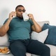 Black guy sitting on a couch in living room drinking a tea and eating a cookies - PhotoDune Item for Sale