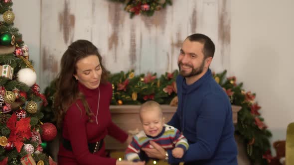 Mother, Father and a Baby Have a Fun in the Room with Christmas Decoration alt