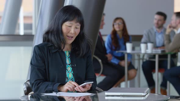 Mature Asian businesswoman using cell phone in office lobby