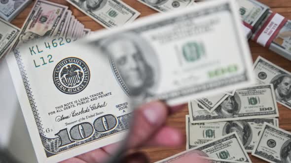 One Hundred Dollars Inspecting Under Magnifying Glass on Money Background alt