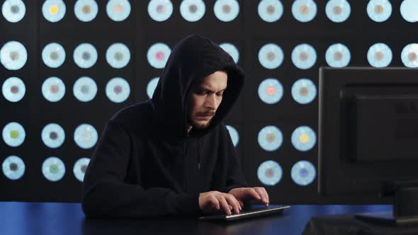 Worried Serious Male Computer Hacker Wearing Black Hoodie Works in Dark Room