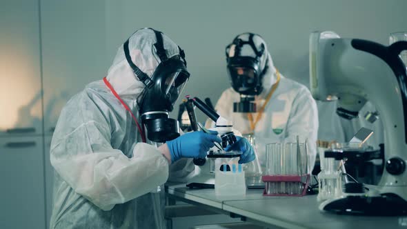 People in Protective Suits Work with Microscopes in Laboratory During Coronavirus Pandemic. alt