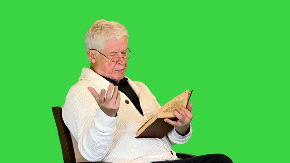 Senior Man Reading Aloud a Book on Camera on a Green Screen Chroma Key alt