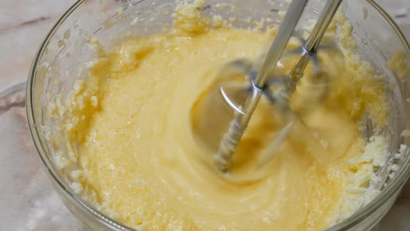 View From Above the Process of Kneading Dough in a Deep Glass Bowl with a Mixer Using Sugar Butter