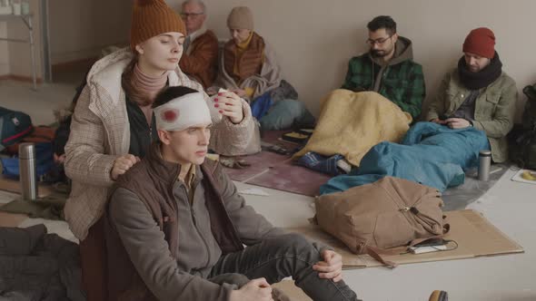 Young Woman Providing First Aid to Refugee Man alt