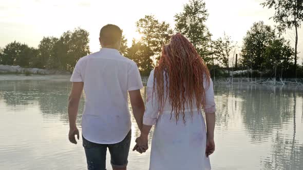 Couple of Lovers at Sunset Go Into the Water of the Lake Holding Hands. Romantic Date. alt