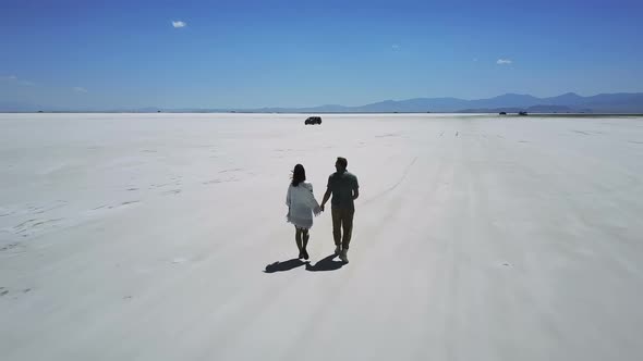 Drone Follows Romantic Couple Holding Hands, Walking Towards Distant Car in the Middle of Bonneville alt
