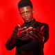 Young black man in stylish attire posing against a vibrant red studio background - PhotoDune Item for Sale