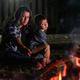 young latin woman carrying her son, sitting in front of a campfire at night, looking sad and bored. - PhotoDune Item for Sale